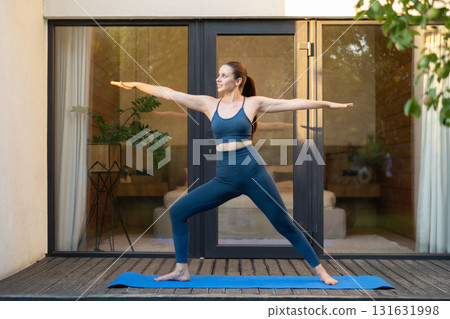 Young woman doing yoga and standing a warrior pose Young woman doing yoga and standing a warrior pose 131631998