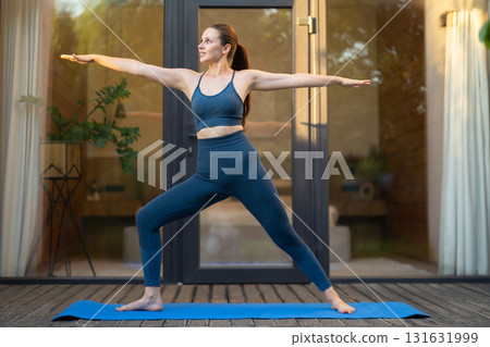 Young woman doing yoga and standing a warrior pose Young woman doing yoga and standing a warrior pose 131631999