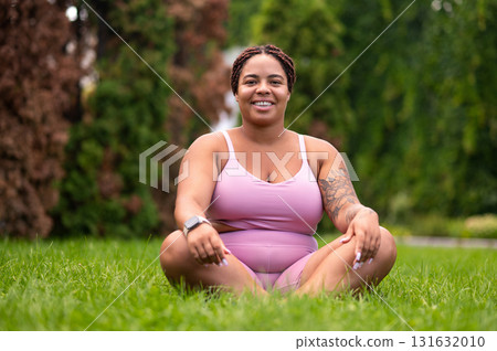Woman in pink sportswear sitting on a grass on lotus pose and feeling good Woman in pink sportswear sitting on a grass on lotus pose and feeling good 131632010