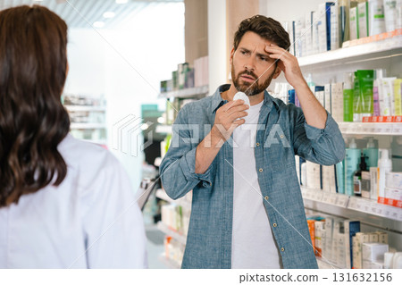 Pharmacist near product shelf and explaining choice for flu treatment to male client 131632156