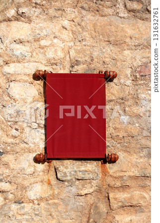 Decorative fabric scroll on a medieval stone wall. Old red textile scroll with rolled edges. Unique, vintage look, adding a touch of history to project. Copy space for text 131632761