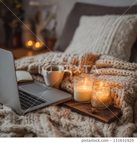 Cozy workspace with laptop, candles, and coffee on knitted blanket for warm ambiance 131632920