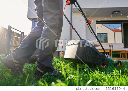 Person mowing grass with electric lawn mower in backyard Person mowing grass with electric lawn mower in backyard 131633044
