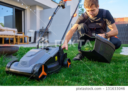 Man cleaning grass container of electric lawn mower 131633046