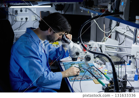 Technician working on circuit board under microscope in lab 131633336