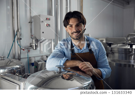 A man wearing an apron is leaning against a large metal container A man wearing an apron is leaning against a large metal container 131633340