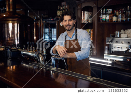 A man brewer is standing behind a bar counter, serving customers 131633362