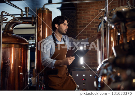 A brewer man worker wearing an apron is diligently working in a local brewery 131633370