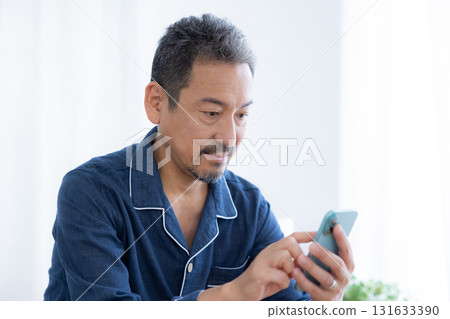 一位穿著睡衣的中年男子正在看他的智慧型手機 一位穿著睡衣的中年男子正在看他的智慧型手機 131633390