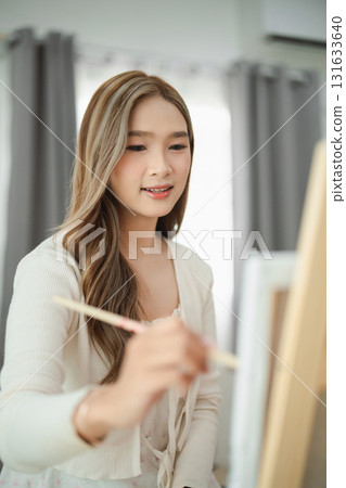 Young woman painting on canvas in bright indoor space, focusing on artwork with a joyful expression, creative hobby and artistic journey captured beautifully 131633640