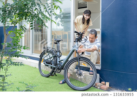 A middle-aged man maintaining an electric bicycle in the garden 131633955
