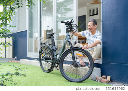 A middle-aged man maintaining an electric bicycle in the garden 131633962