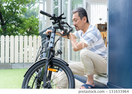 A middle-aged man maintaining an electric bicycle in the garden A middle-aged man maintaining an electric bicycle in the garden 131633964