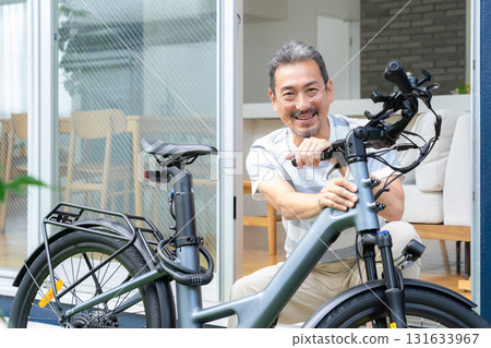 A middle-aged man maintaining an electric bicycle in the garden 131633967