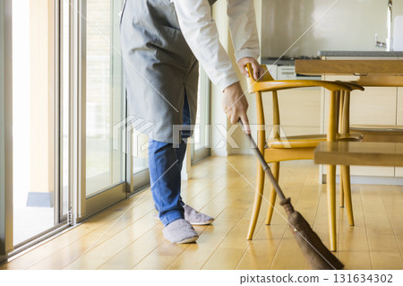 A man cleaning the living room with a broom 131634302