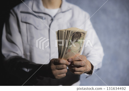 A man in work clothes counting 10,000 yen bills A man in work clothes counting 10,000 yen bills 131634492