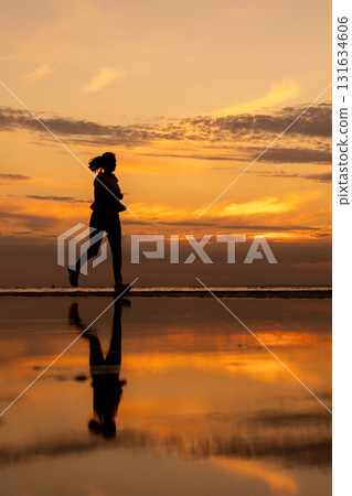 Silhouette of woman doing sports by the sea during an amazing sunset, jogging. 131634606