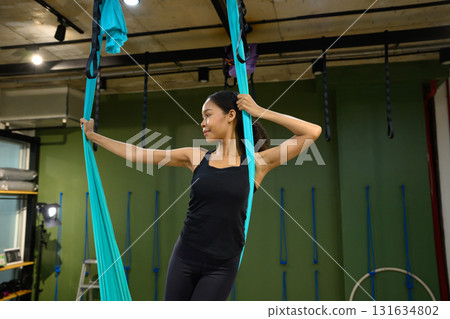 Young woman practicing aerial yoga using hammock straps during a wellness workout session 131634802