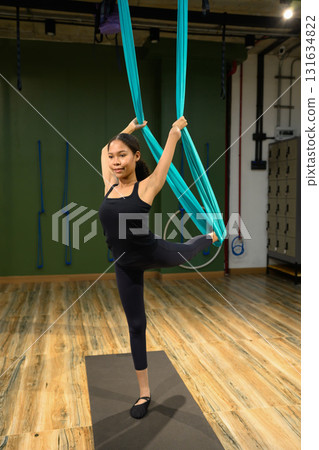 Young woman practicing aerial yoga pose with hammock support for balance and flexibility improvement Young woman practicing aerial yoga pose with hammock support for balance and flexibility improvement 131634822
