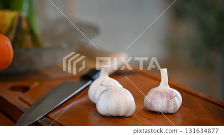 Close up of garlic heads placed on a wooden surface with kitchen knife 131634877