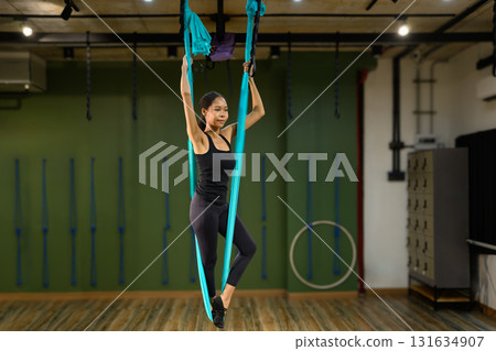 Young woman practicing aerial while holding the fabric straps in a professional yoga studio Young woman practicing aerial while holding the fabric straps in a professional yoga studio 131634907