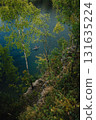 Kayaker gliding across serene lake, framed by birch trees atop cliff, embracing tranquility and beauty of nature in picturesque outdoor landscape. Kayaker navigating calm lake waters. Natural beauty 131635224