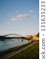 Old bridge crossing Vistula river in Krakow, Poland, during sunset with blue sky and some clouds, view from riverbank with grass and pedestrian path. Bridge spanning Vistula river in Krakow, Poland 131635233