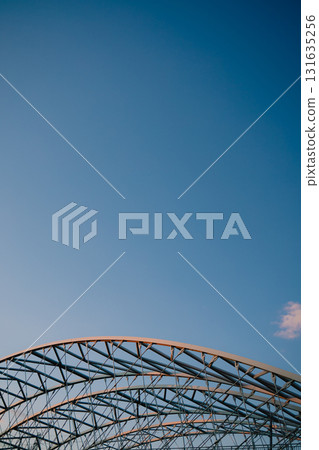 Vertical screen: curved metal beams creating robust and intricate framework rise against clear blue sky, highlighting elegance of industrial design and contemporary architecture. Modern architecture 131635256