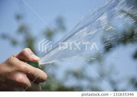 A man's hand holds a watering hose and closes the hole with his thumb A man's hand holds a watering hose and closes the hole with his thumb 131635346