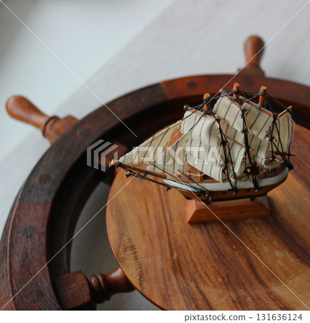 A scale model of an old sailing ship sits on the wooden center of a ship's steering wheel on a shelf A scale model of an old sailing ship sits on the wooden center of a ship's steering wheel on a shelf 131636124
