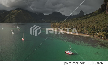 Stunning aerial view of yachts in turquoise lagoon bay, tropical island beach in French Polynesia, green mountains and dramatic cloudy sky. Remote wild nature paradise, exotic summer travel background 131636975