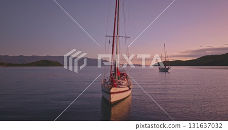 Two sailboats floating on calm ocean water bay during vibrant sunset and silhouetted hills. Travel, tourism, holiday, relax, active lifestyle Amazing nature landscape, remote destination. Drone flight Two sailboats floating on calm ocean water bay during vibrant sunset and silhouetted hills. Travel, tourism, holiday, relax, active lifestyle Amazing nature landscape, remote destination. Drone flight 131637032