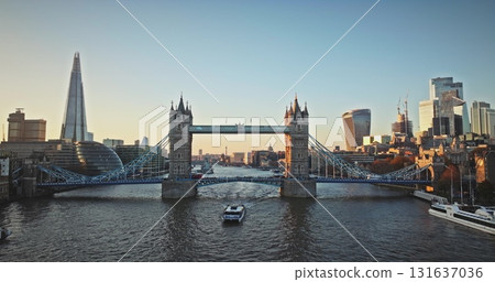 England, London: Aerial view tourist boat sailing River Thames under Tower Bridge, with The Shard and City of London skyline in the background during a beautiful bright sunset. Drone flight England, London: Aerial view tourist boat sailing River Thames under Tower Bridge, with The Shard and City of London skyline in the background during a beautiful bright sunset. Drone flight 131637036