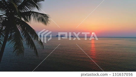 Beautiful sunset over the calm sea creating warm colors reflecting on the water surface with palm tree silhouette and islands on the horizon in Koh Samui, Thailand 131637056