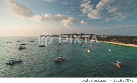 Aerial view capturing Cagban Beach in Boracay, Philippines, filled with bangka boats gliding across vibrant turquoise waters under a sunny sky with white clouds 131637072