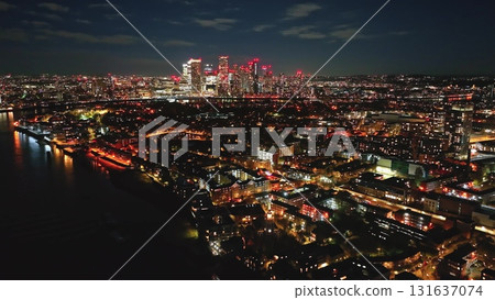 England, London: Breathtaking aerial view of London at night, featuring the illuminated Canary Wharf skyline, creating a mesmerizing cityscape reflecting in the River Thames. Drone flight England, London: Breathtaking aerial view of London at night, featuring the illuminated Canary Wharf skyline, creating a mesmerizing cityscape reflecting in the River Thames. Drone flight 131637074