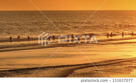 Fishermen casting rods into the ocean waves fishing during stunning sunset in Bali, Indonesia, create a breathtaking golden orange seascape, tropical tranquility. Beautiful nature travel background 131637077