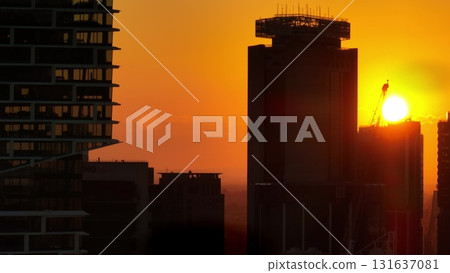 Australia, Sydney: Modern city architecture background. Stunning orange sunset over city skyline with construction crane silhouette and vibrant evening sky creating dramatic evening cityscape 131637081