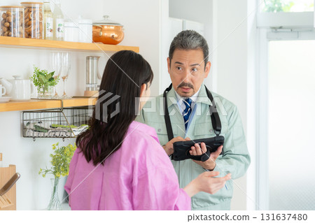 A real estate agent and a middle-aged woman doing maintenance in the kitchen A real estate agent and a middle-aged woman doing maintenance in the kitchen 131637480