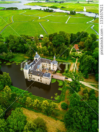 Aerial view of historic castle with moat, four corner towers, and circular garden nestled in lush greenery and water channels, blending elegance with rural tranquility. 131637621