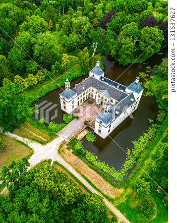 Aerial view of forested estate with symmetrical castle, moat, and bridge two front towers frame a central courtyard, blending historical architecture with lush natural surroundings. 131637627