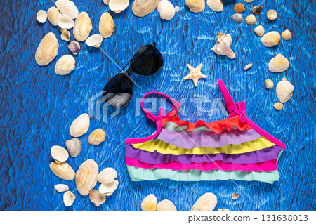 A collection of travel items including suitcase, sunglasses, swim suit, sunscreen and shells on turquoise navy blue background 131638013