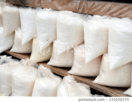 Large pellets of white raw salt packed in clear plastic bags stacked on wooden shelves 131638174