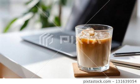 Iced latte in a glass on a modern office desk with laptop and notepad, refreshing drink for workspace Iced latte in a glass on a modern office desk with laptop and notepad, refreshing drink for workspace 131639354