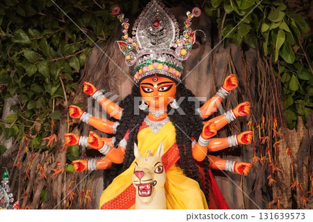 Close up of Goddess Durga Idol with Orange Face and Natural Banyan Tree Pandal Close up of Goddess Durga Idol with Orange Face and Natural Banyan Tree Pandal 131639573