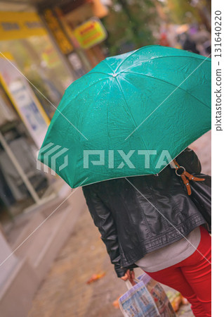 Woman rushing with green teal umbrella on rainy urban street. Intentional rotation of angle towards horizon. Concept of autumn weather, lifestyle, city rain mood, street life in motion Woman rushing with green teal umbrella on rainy urban street. Intentional rotation of angle towards horizon. Concept of autumn weather, lifestyle, city rain mood, street life in motion 131640220