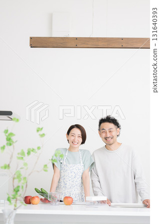 A middle-aged couple looking at the camera and smiling in the kitchen 131640393
