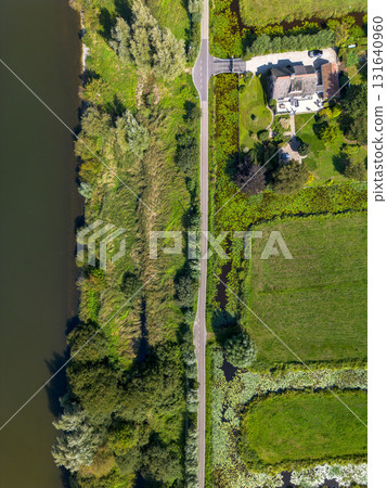 Aerial view of river bordered by forest and farmland, with a vertical road dividing lush vegetation and rectangular fields highlighting land use and ecological contrast. 131640960