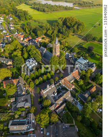 Aerial view of town with central Gothic style church, pointed steeple, red and gray rooftops, tree lined streets, and parked cars blending history with modern life. 131640962