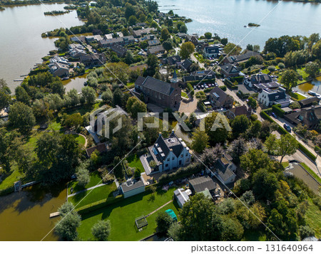 Aerial view of a small town with a central church and tall steeple, surrounded by houses, tree lined streets, and nearby lakes with islands, blending historic charm and natural beauty. 131640964